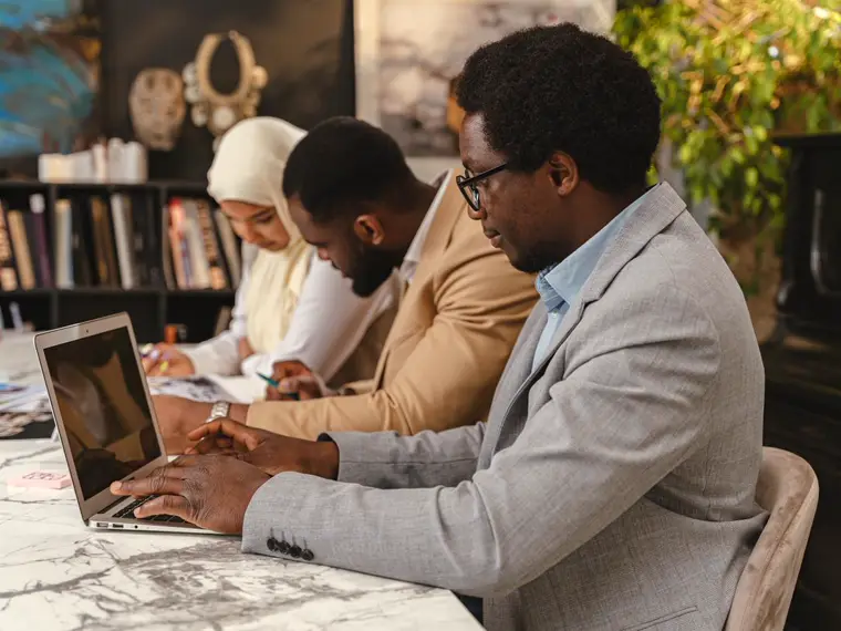 Trois professionnels au travail dans un bureau, ordinateur portable et documents.
